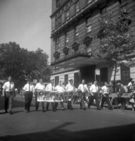Labor Day, Shoot ID: 406, Negative 12. Image of a black and white photograph. In the photograph, a group of men in matching uniforms walk down a street with a banner labeled "Officers Local Union I.B.E.W." (part of the banner's text is covered and unclear). A small crowd watches from behind a police line on the sidewalk. In the background, there are several trees and a large building. Full text includes "Officers Local Union I.B.E.W."