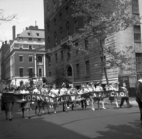 Labor Day (Other Street Scenes), Shoot ID: 410, Negative 10. Image of a black and white photograph. In the photograph, a group of women with hats and US flags carry a large banner down a street. The banner says "Local 66 I.L.G.W.U. A.F.L.-C.I.O." Behind the women with the banner, there is a large crowd of people following with posters. In the background, there are several tall buildings. Full text includes "Local 66 I.L.G.W.U. A.F.L.-C.I.O."