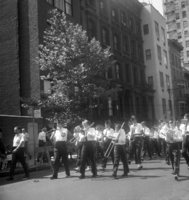 Labor Day, Slogans include "Pass Anti-Scab Legislation" and "TWU Supports Freedom Riders", Shoot ID: 416, Negative 30. Image of a black and white photograph. In the photograph, a band of boys walks down a street. A crowd watches from the sidewalk. There are several buildings in the background. 
